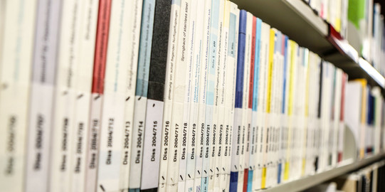 Dissertationen in der Bibliothek Bücher mit der Aufschrift Dissertation auf dem Buchrücken im Bücherregal der Bibliothek
